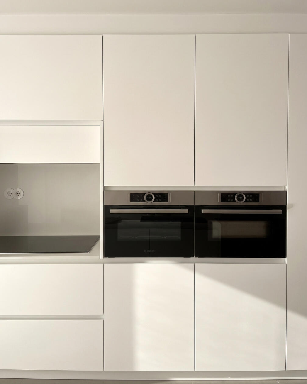 Cozinha contemporânea com armários brancos de linhas lisas, eletrodomésticos integrados e bancada clara.
